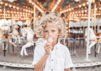 Childhood Innocence: Curly-haired Boy with Lollipop at Carousel, Moments of Joy in Summer Funfair