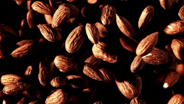 A closeup of a pile of brown almonds on a black background, with a natural wood pattern. These natural foods are sourced from a singleorigin coffee event