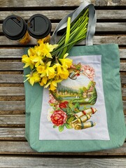 bouquet of yellow daffodils and cups of coffee on a bag with embroidery