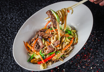 The image is of a bowl of stir-fried noodles, a popular Chinese dish. It includes various...