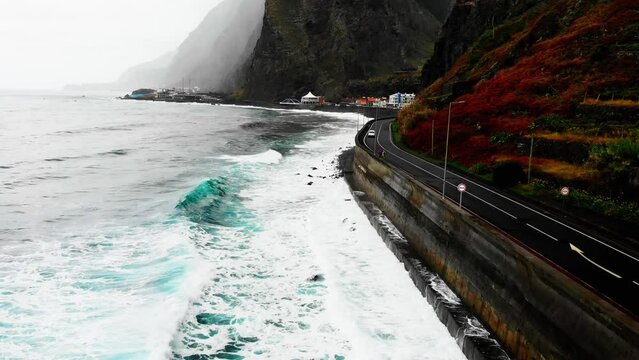The drone captures a tumultuous storm over the ocean near the road, with powerful waves crashing against the shore, creating a dramatic and awe-inspiring scene