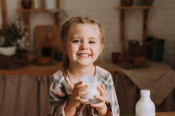 Cute little girl in the kitchen drinking yogurt and eating a bun
