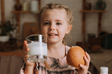 Cute little girl in the kitchen drinking yogurt and eating a bun