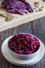 Homemade pickled red cabbage in white ceramic bowl. Vertical, close up