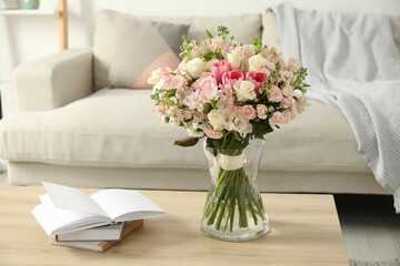 Beautiful bouquet of fresh flowers in vase and books on wooden table indoors