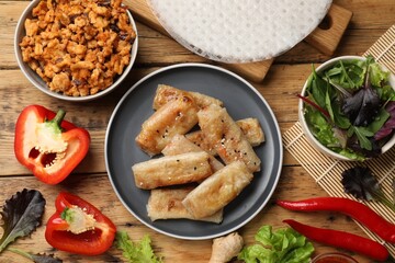 Tasty fried spring rolls and ingredients on wooden table, flat lay