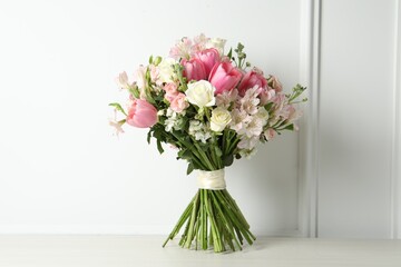 Beautiful bouquet of fresh flowers on table near white wall