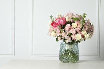 Beautiful bouquet of fresh flowers in vase on table near white wall. Space for text