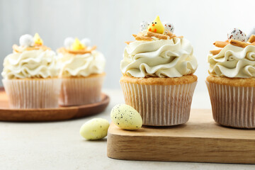 Tasty Easter cupcakes with vanilla cream and candies on gray table, selective focus