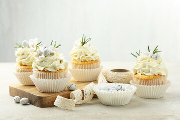 Tasty Easter cupcakes with vanilla cream, candies and ribbon on gray table