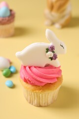 Tasty cupcake with Easter decor on pale yellow background, closeup