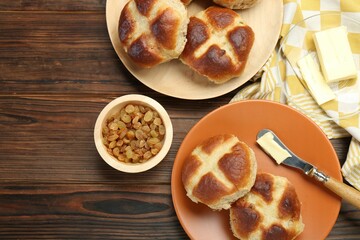 Tasty hot cross buns, knife with butter and raisins on wooden table, flat lay. Space for text
