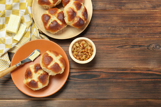 Tasty hot cross buns, knife with butter and raisins on wooden table, flat lay. Space for text
