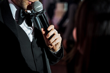 A man in formal wear gestures with microphone towards a woman at an event