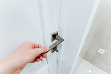 Man holding the door handle with his hand, opening the door by the handle, white door to the room.