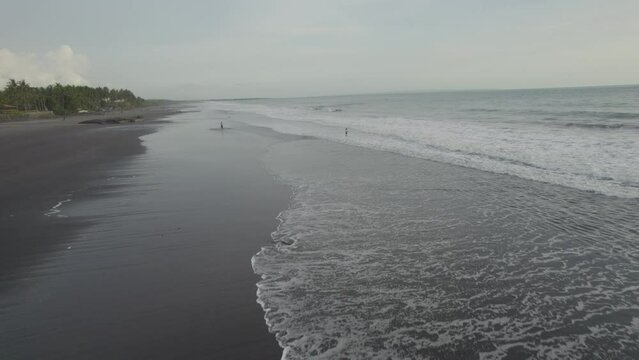 A beach with a few people walking on it. The sky is cloudy and the beach is mostly empty