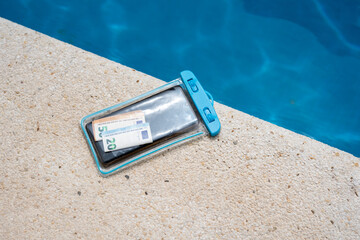 Waterproof case with money and a smartphone on the background of the pool on a sunny summer day