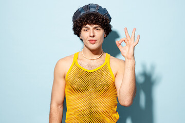 Young happy gay Latin man wear mesh tank top hat clothes showing okay ok gesture look camera isolated on plain pastel light blue cyan background studio portrait Pride day June month love LGBT concept