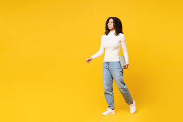 Fototapeta na wymiar Full body smiling fun little IT kid teen girl of African American ethnicity wear white casual clothes hold laptop pc computer go isolated on plain yellow background studio Childhood lifestyle concept