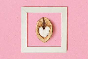 Half of heart shaped walnut in white frame on pink background - Concept of love and heart health benefits of walnuts