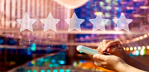 Rating star concept with person using a smartphone in a city at night - 781913340