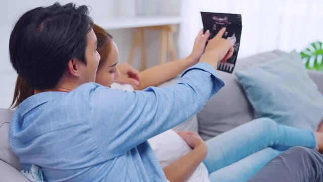 Asian young couple watching ultrasound pregnancy test photo in bedroom. 