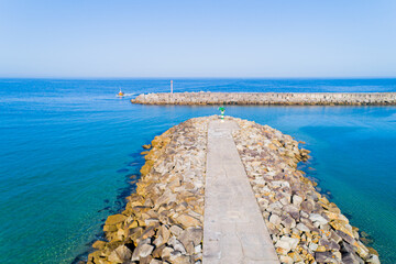 photo of a breakwater at the entrance of a harbor and a ship arriving at the port.