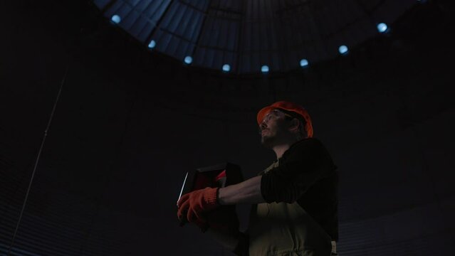 Male worker in safety helmet with flashlight in hands inside storage tank. Inside the grain silo.