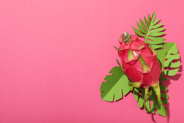 One whole dragon fruit and paper tropical leaves on pink background, space for text