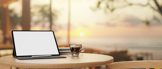 A digital tablet mockup on a wooden round table with a blurred background of a sunset beach view.