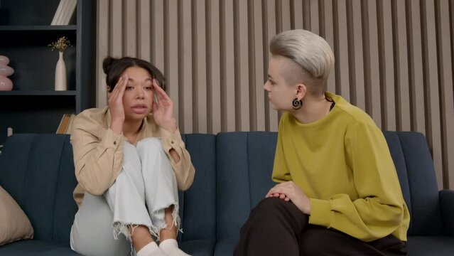 Caring female counselor giving psychological help to depressed anxious African American woman patient, seated with arms around knees on couch, to mitigate troublesome behaviors and overcome problems.