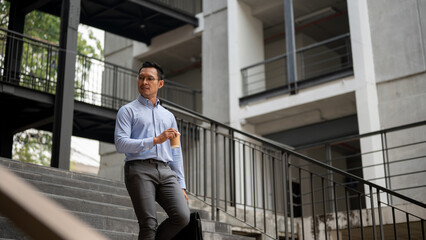 A confident, determined Asian businessman walking down the stairs, looking away from the camera.