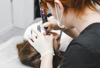 A cosmetologist applies permanent makeup to the eyebrows - eyebrow tattoo. eyebrow perm