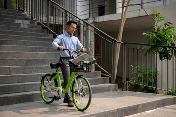 A focused Asian businessman pushing a green bicycle in the city, going to work with his bicycle.