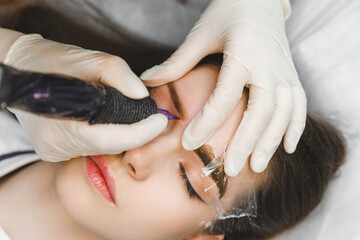 A cosmetologist applies permanent makeup to the eyebrows - eyebrow tattoo. eyebrow perm