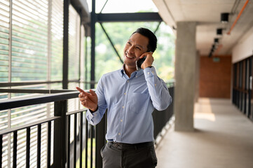 A confident Asian businessman talking on the phone with his client while walking on a corridor.