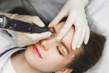 Fototapeta premium A cosmetologist applies permanent makeup to the eyebrows - eyebrow tattoo. eyebrow perm
