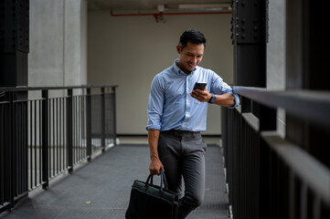 A handsome Asian businessman checking messages on his phone while standing on an outdoor corridor.