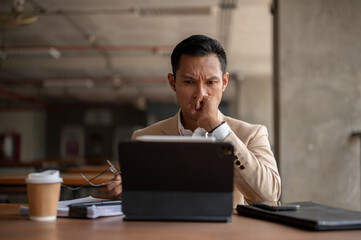 An Asian businessman is staring at his tablet screen with a serious expression, facing a problem.