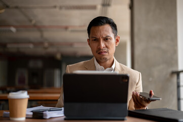 A confused Asian businessman is staring at his digital tablet screen with a puzzled expression.