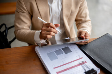 A businessman in a beige suit using his digital tablet and reviewing business document at a table.