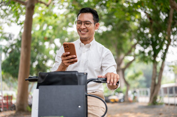 A happy, carefree Asian businessman is checking messages on his smartphone while he is on a bike.