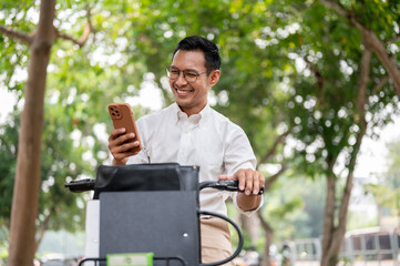 A happy, carefree Asian businessman is checking messages on his smartphone while he is on a bike.