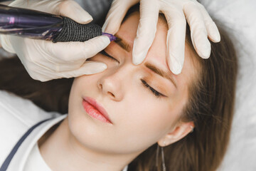 Fototapeta premium A cosmetologist applies permanent makeup to the eyebrows - eyebrow tattoo. eyebrow perm