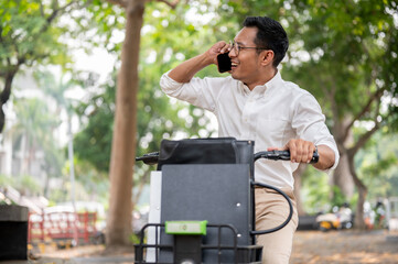 A happy Asian businessman is talking on the phone while he is on a bike, riding a bike to work.