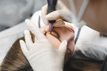 A cosmetologist applies permanent makeup to the eyebrows - eyebrow tattoo. eyebrow perm