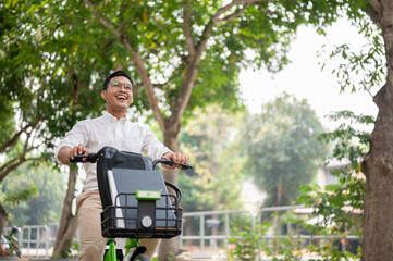 A happy, carefree Asian businessman is on a bike in the park, riding a bike to work in the morning. - 781923190