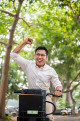 An excited Asian businessman rides a bike triumphantly, raising his fist in celebration. - 781923197