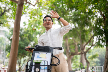 A happy businessman smiles and waves while pushing his bike, greeting someone while heading to work.
