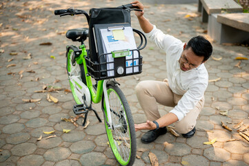 A focused businessman inspects his bicycle tire in a park, encountering an issue during his commute.